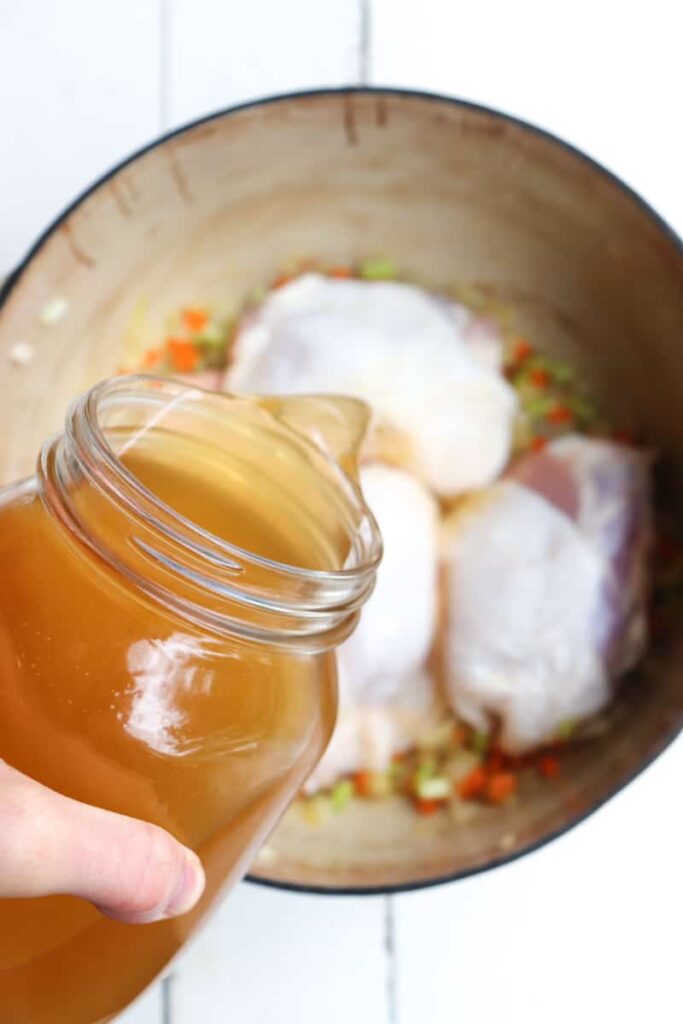 broth being poured over chicken thighs