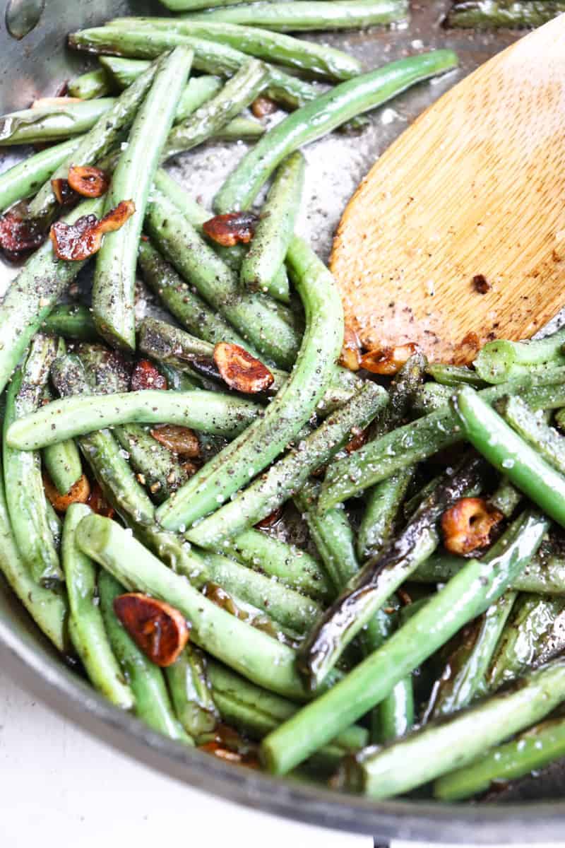 finished green beans in a saute pan with lots of fresh cracked pepper and a wooden spoon