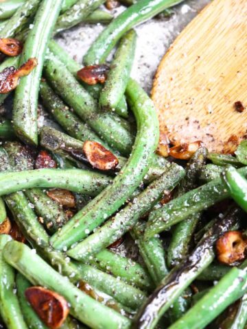 green beans sauteed in pan with a wooden spoon.