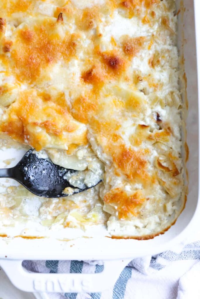 baked potatoes au gratin in a white serving dish with a black spoon 