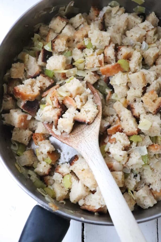 finished leek stuffing in a saute pan with a wooden spoon taking a scoop