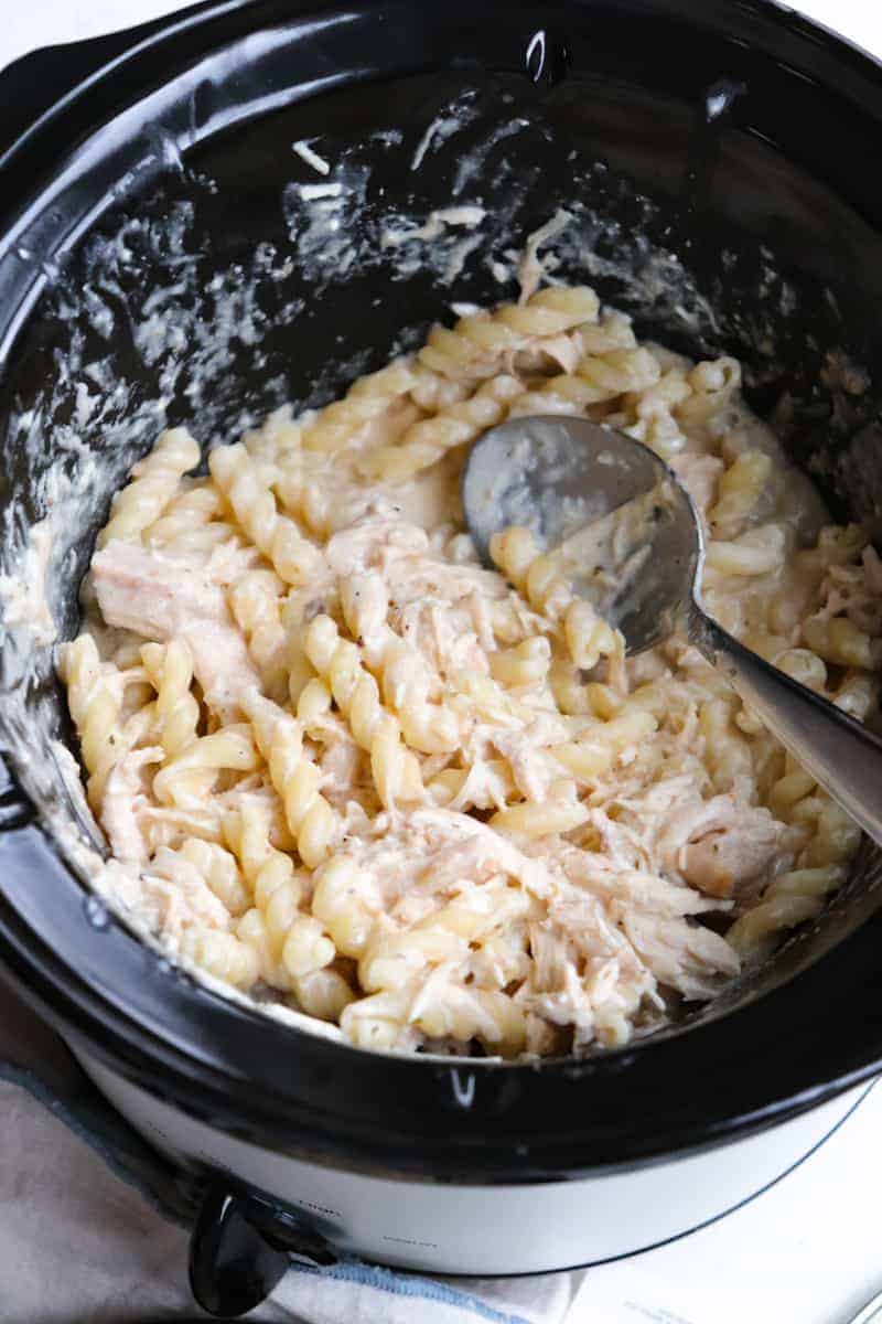 finished olive garden chicken pasta in a crockpot with a metal spoon in the crockpot to scoop 