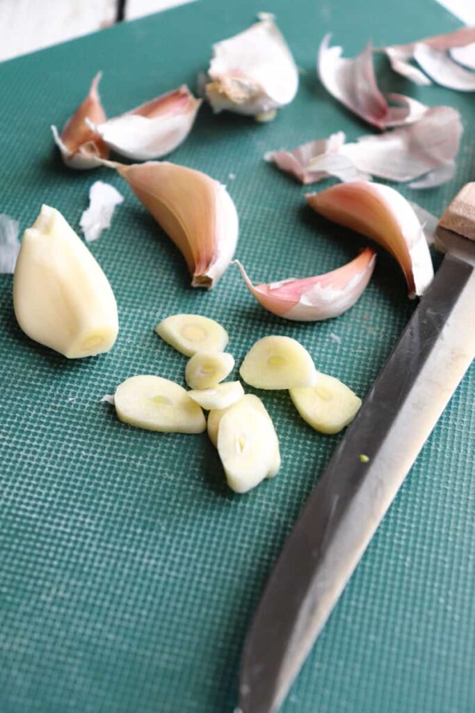 sliced garlic and other garlic cloves on a green cutting board  