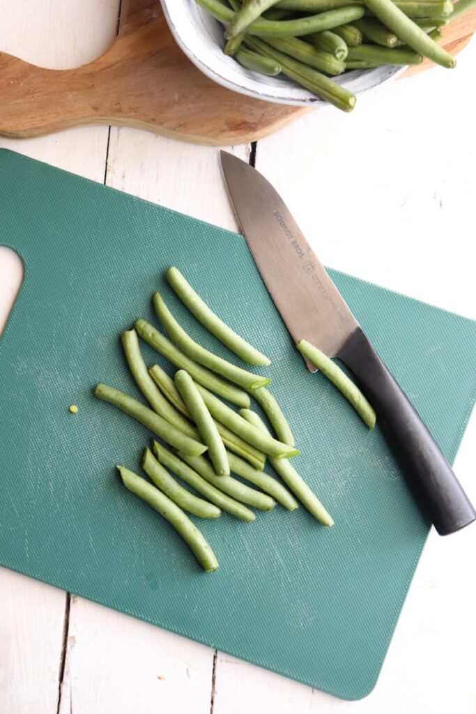 green beans in the process of being trimmed on a green cutting board
