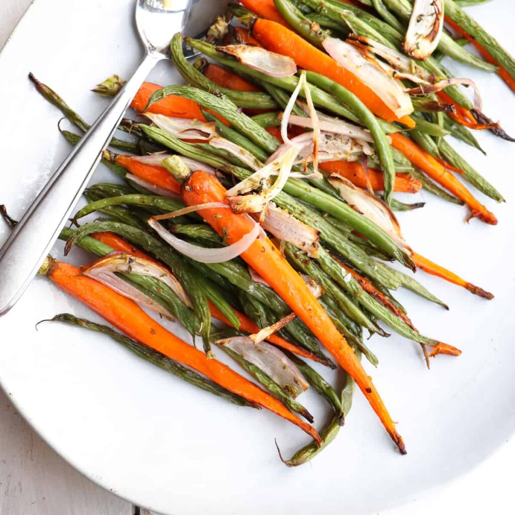 carrots and green beans on a white plate with a metal spoon