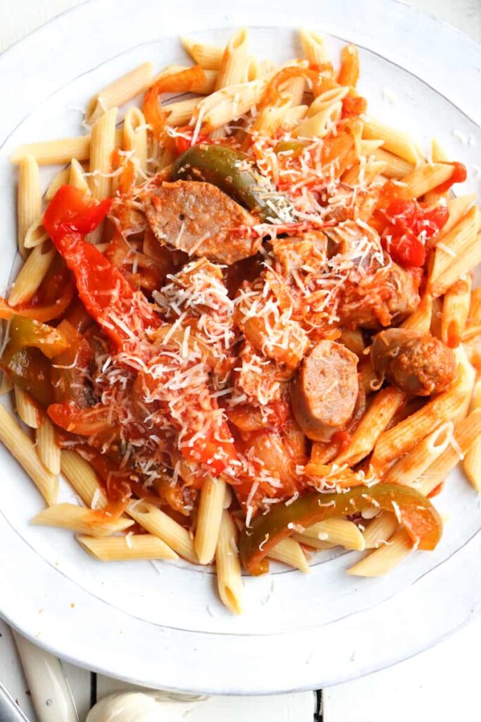 sausage and peppers with penne pasta on a white plate sprinkled with cheese