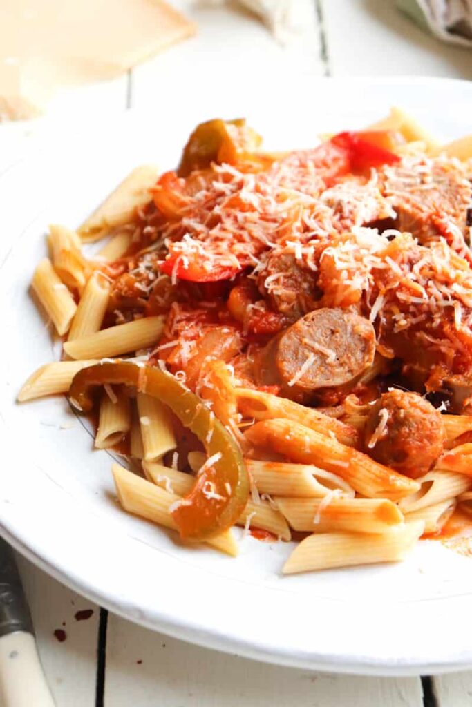 sausage and peppers with penne pasta on a white plate