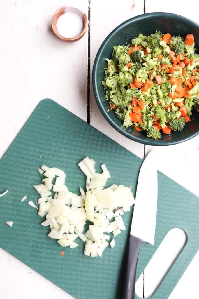diced carrots on a green cutting board with a bowl of carrots and broccoli to the side
