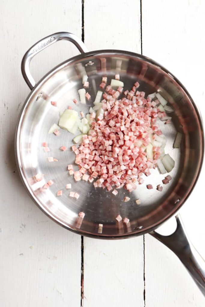uncooked pancetta and diced onions in a stainless steel pan