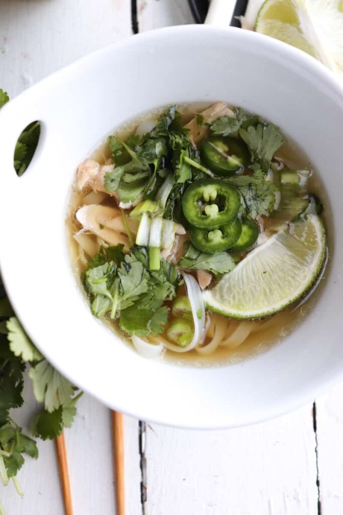 chicken pho topped with herbs in a white bowl