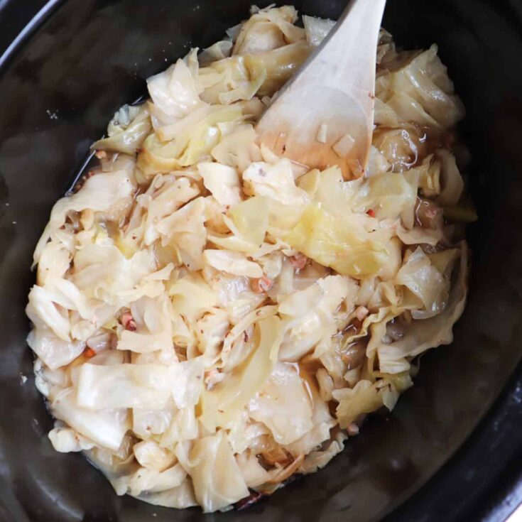 cooked cabbage in the slow cooker with a wooden spoon coming out