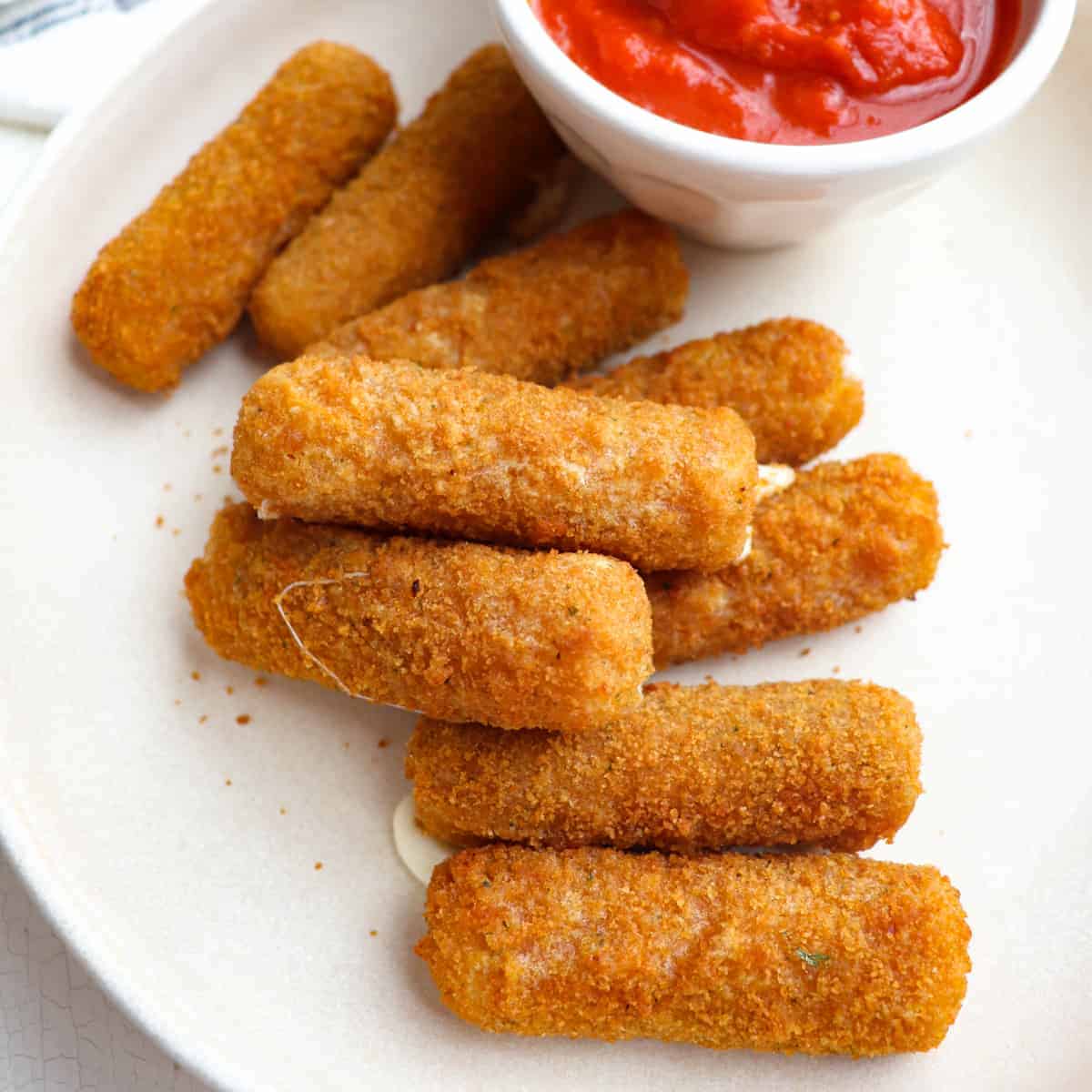 a pile of mozzarella sticks on a plate with a cup of marinara sauce