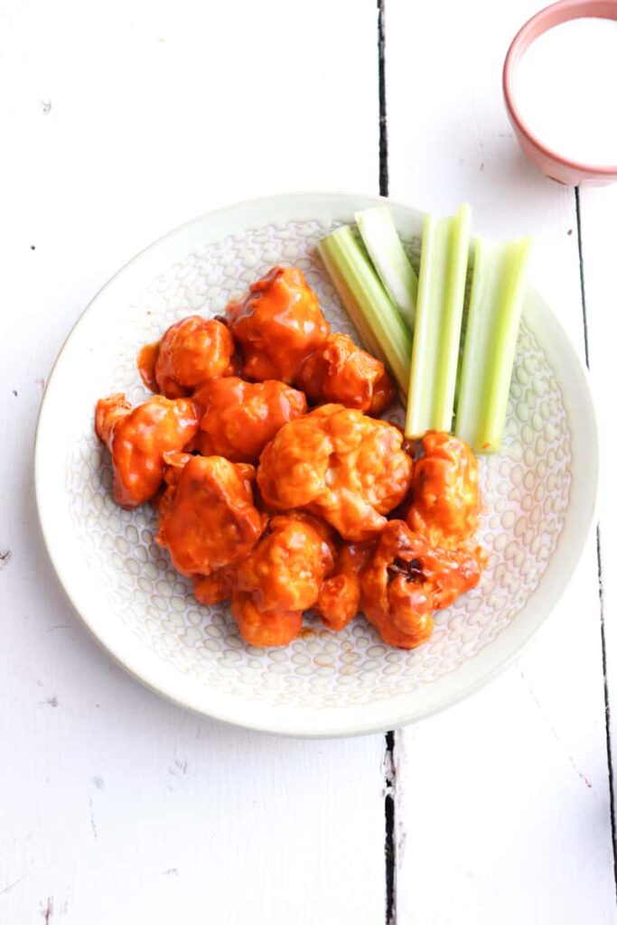 air fryer buffalo wings plated with celery with sauce in the background.