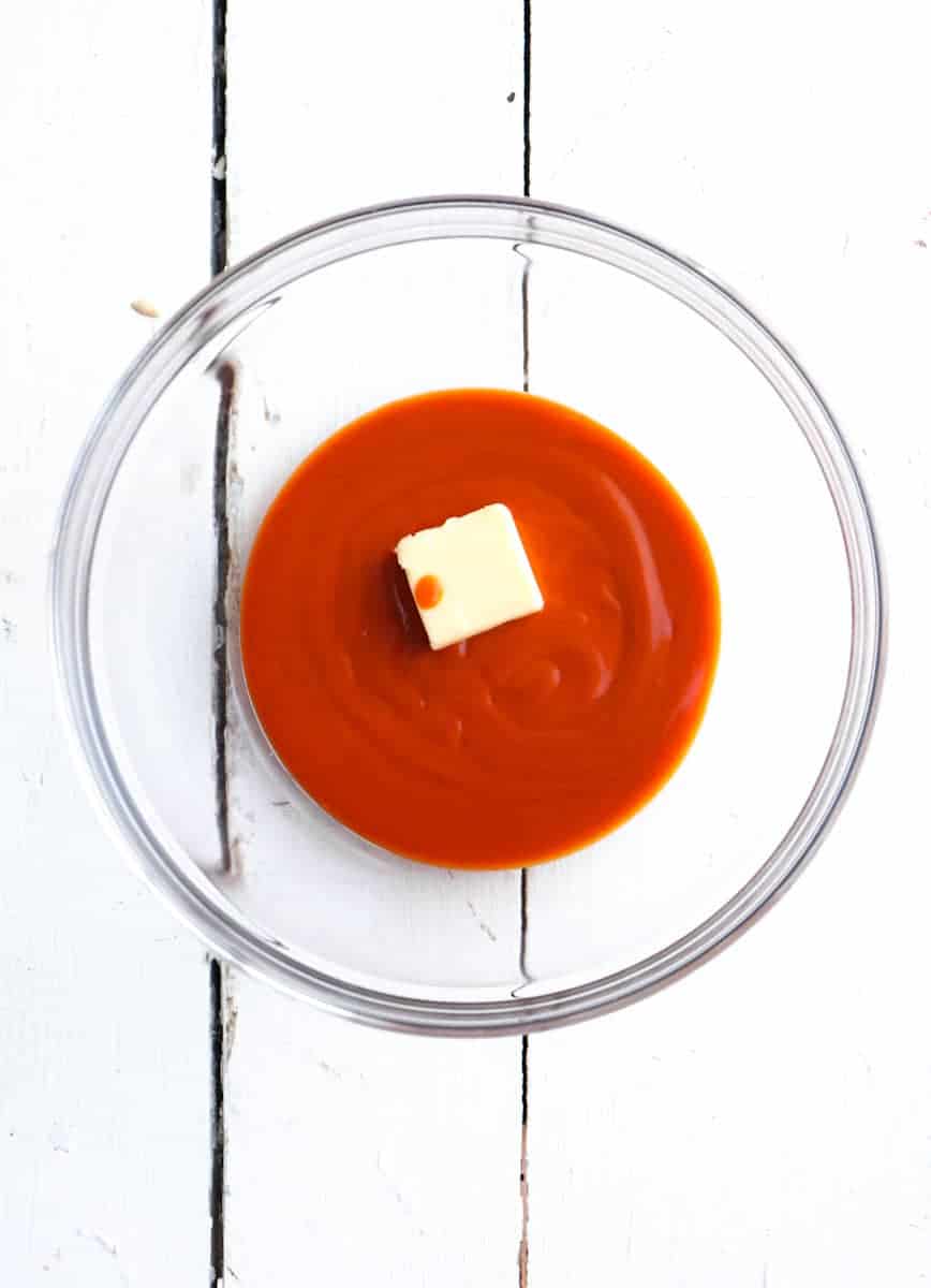 clear glass bowl with buffalo sauce and a pad of butter