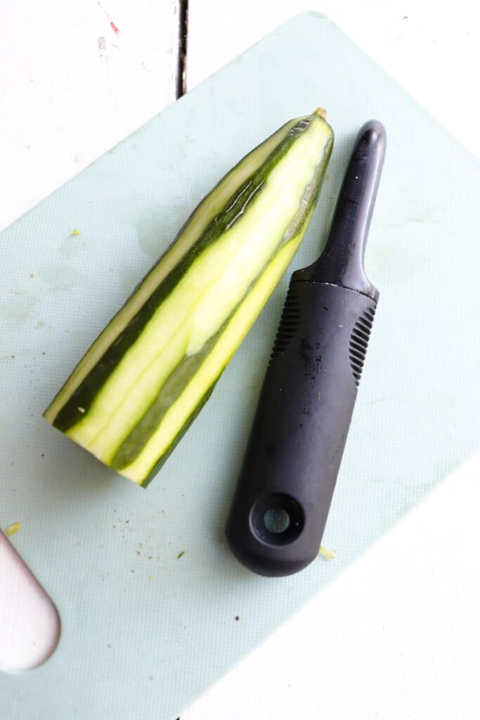 partially peeled cucumber with peeler next to it