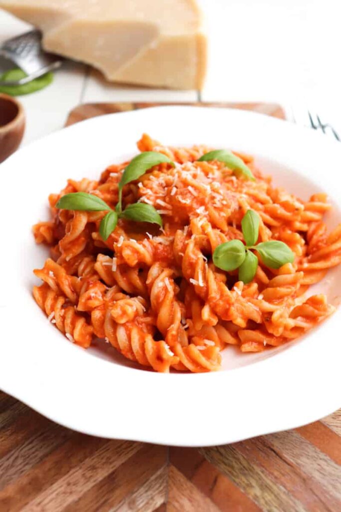 spicy fusilli arrabiata plated in a white bowl with cheese and basil in the background