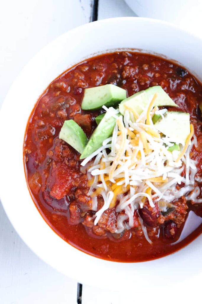 venison chili topped with cheese and avocado in a white bowl