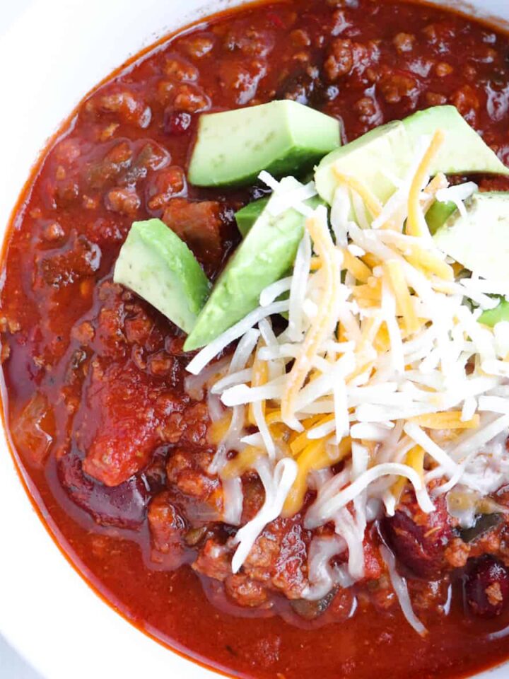 venison chili topped with cheese and avocado in a white bowl