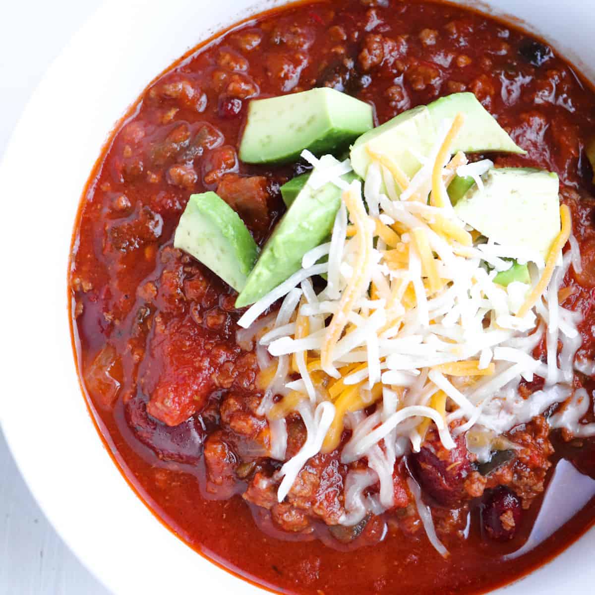 venison chili topped with cheese and avocado in a white bowl