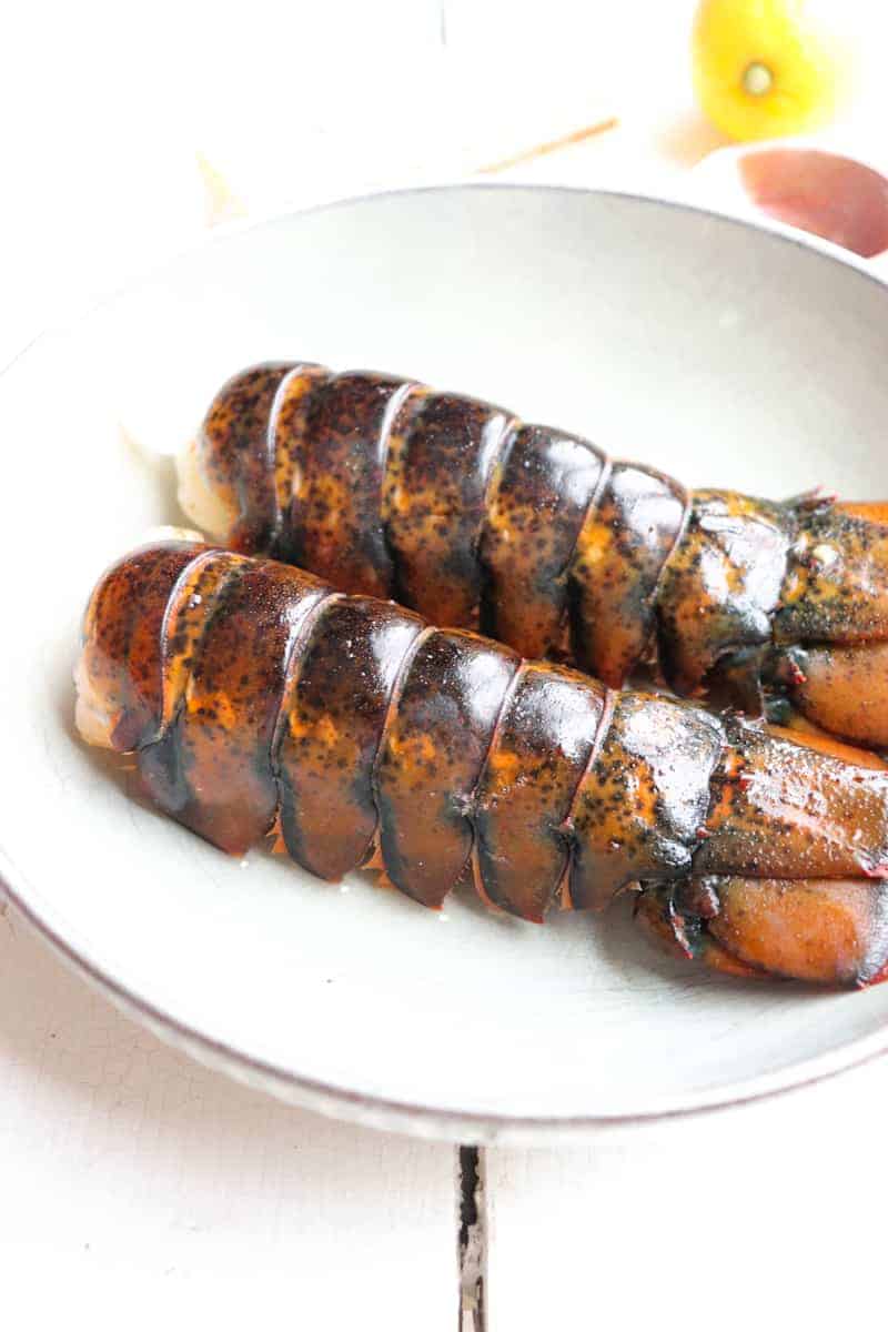 two lobster tails side by side on a grey plate