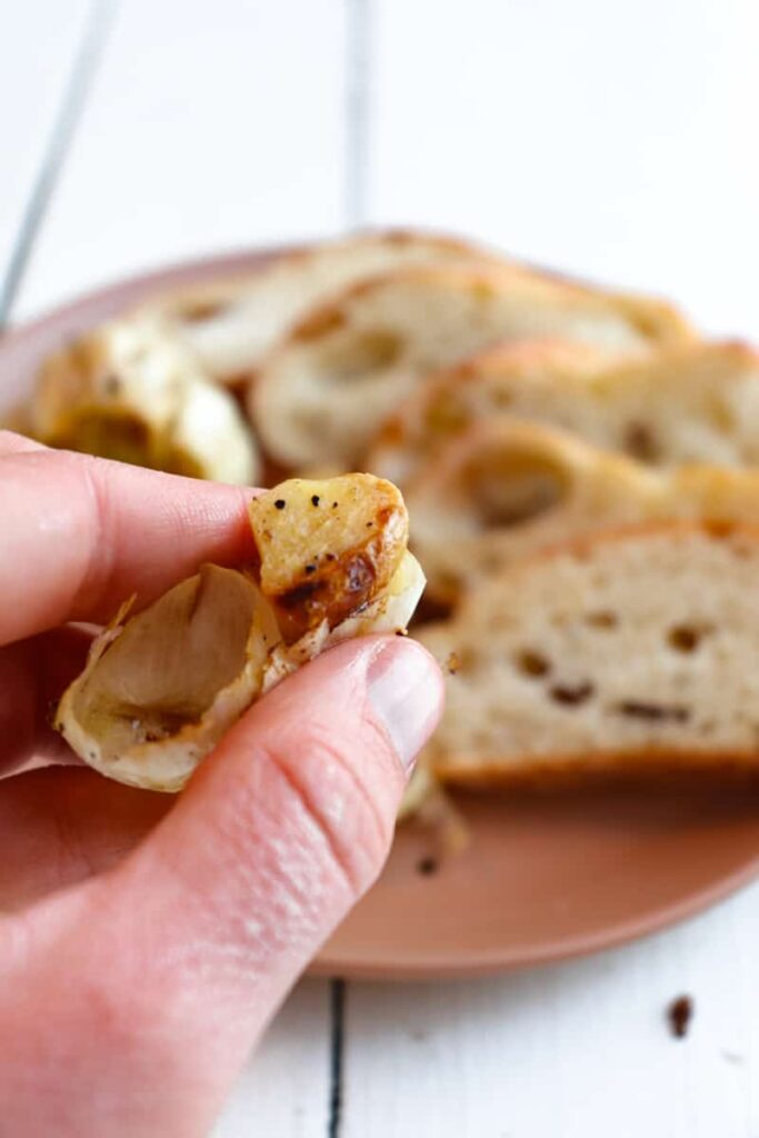 hand popping one garlic clove out of paper