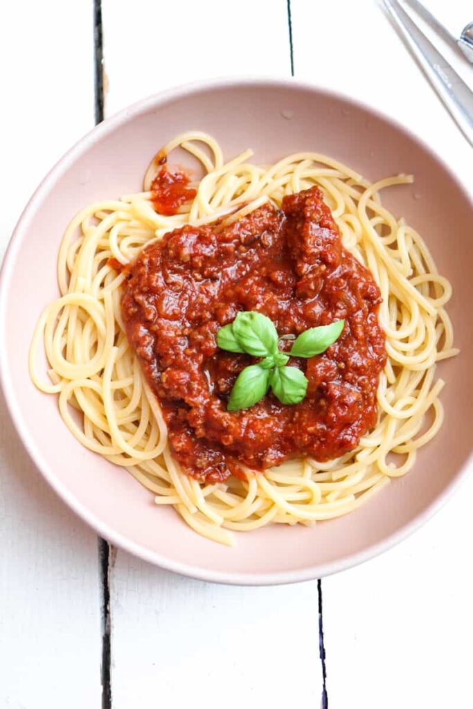 venison ragu on bed of spaghetti topped with basil in a low bowl