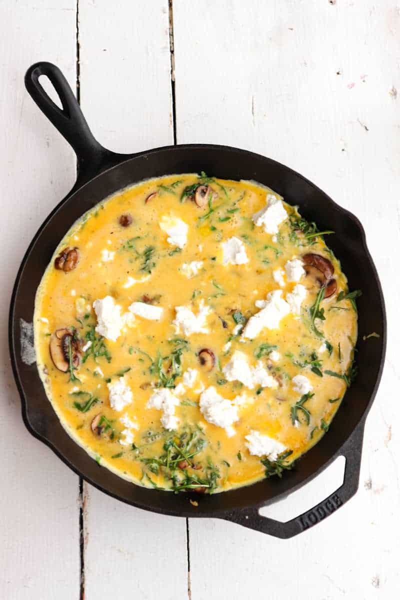 uncooked frittata in skillet with goat cheese added
