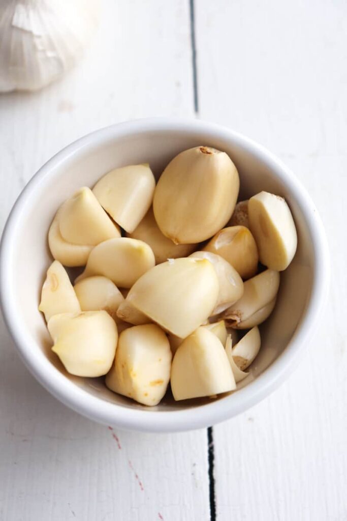 small white bowl filled with peeled garlic cloves