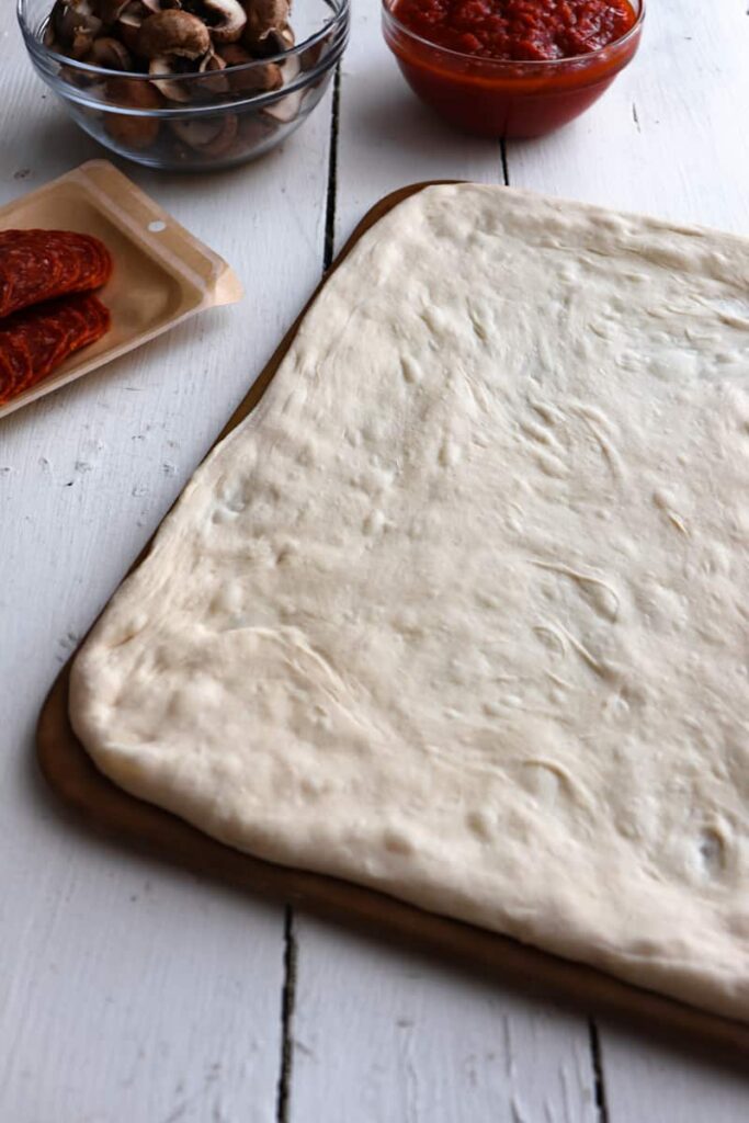 pizza dough stretched into a rectangle on a baking stone