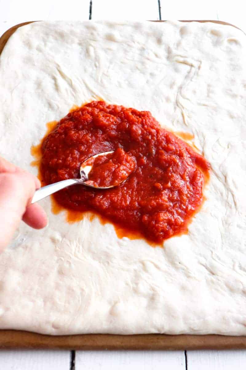 spoon spreading pizza sauce on to dough