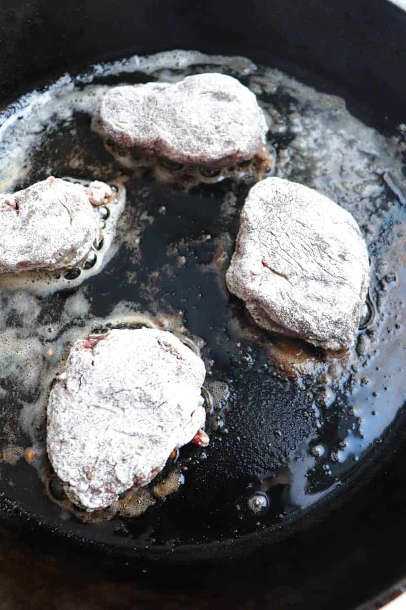 venison medallions coated in flour frying in cast iron skillet