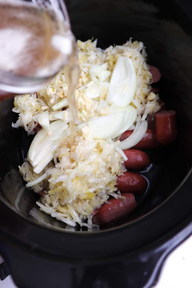 beer pouring into crockpot full of ingredients.