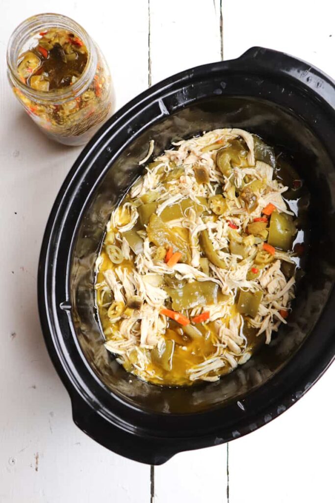 finished giardiniera chicken in the crockpot with jar of hot peppers to the side