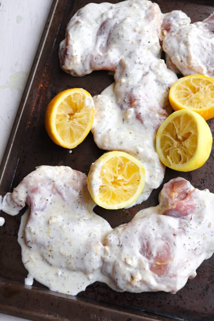 raw marinated chicken thighs and cut lemons on a baking sheet