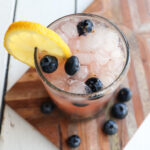 blueberry mocktail in a clear glass garnished with lemon