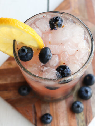 blueberry mocktail in a clear glass garnished with lemon