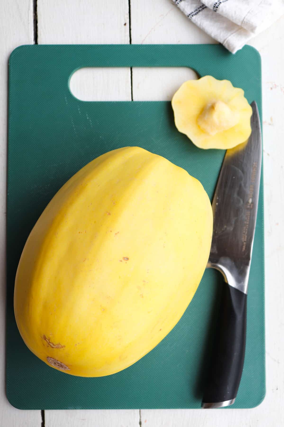 squash sitting on green cutting board with stem trimmed off.
