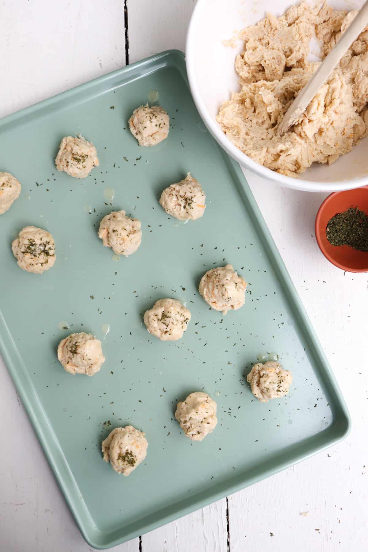uncooked biscuits on green baking sheet.
