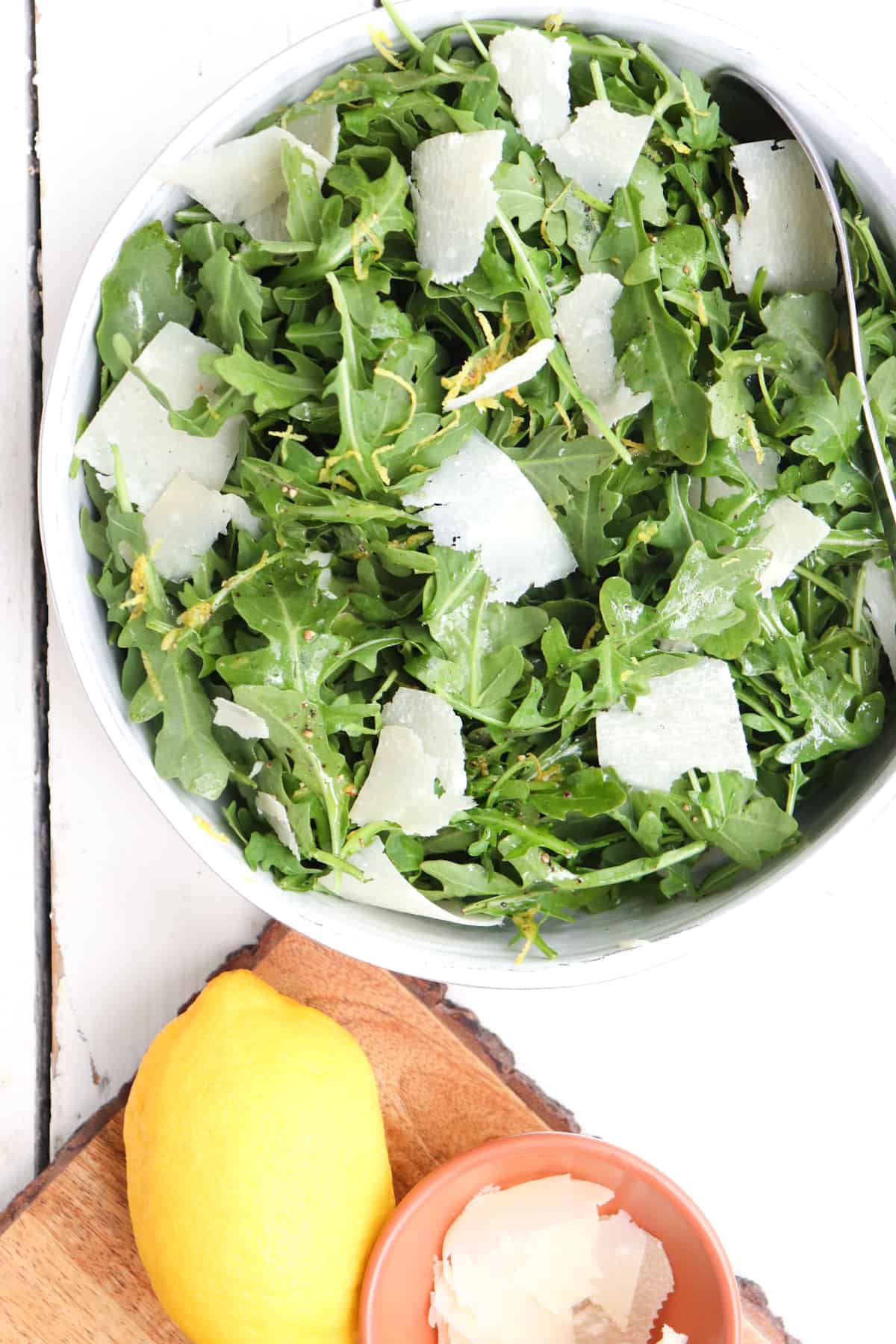 arugula salad with shaved parmesan in a white bowl.