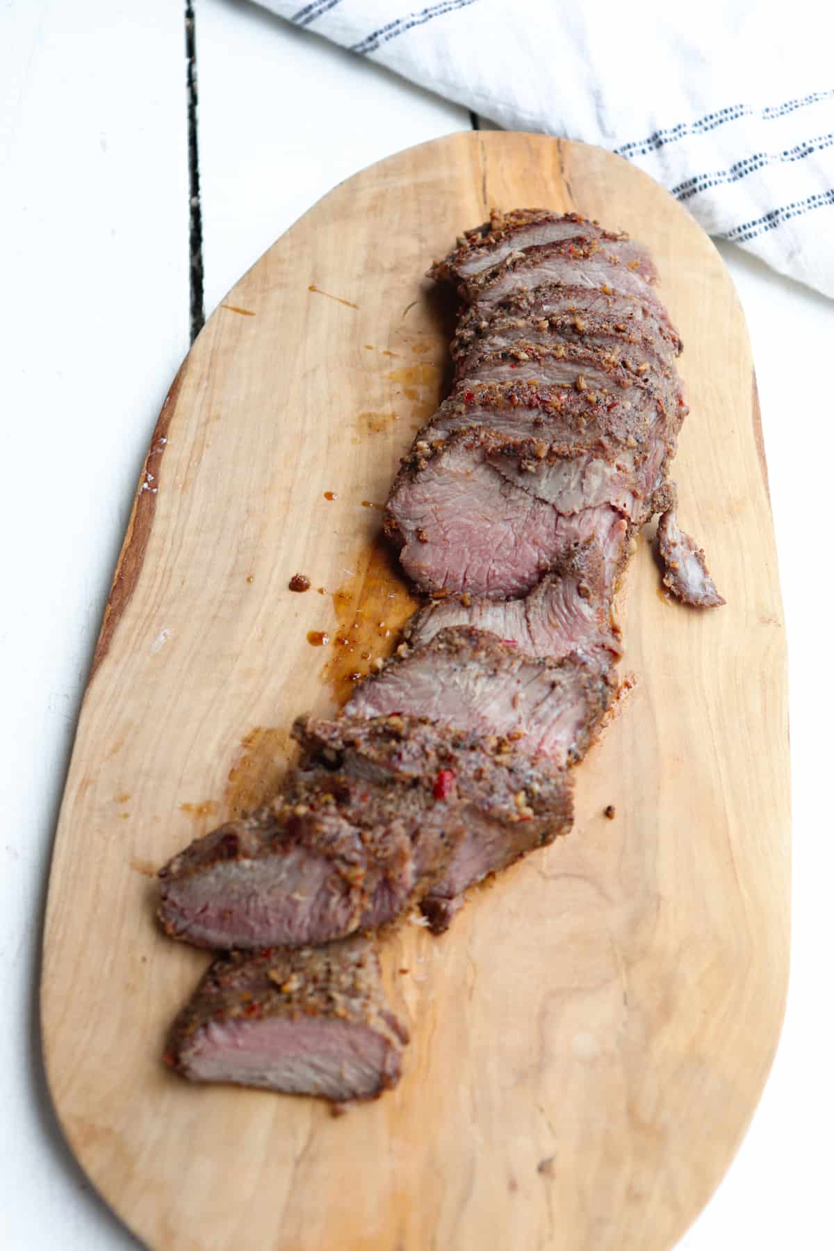 sliced sous vide venison on wooden cutting board.
