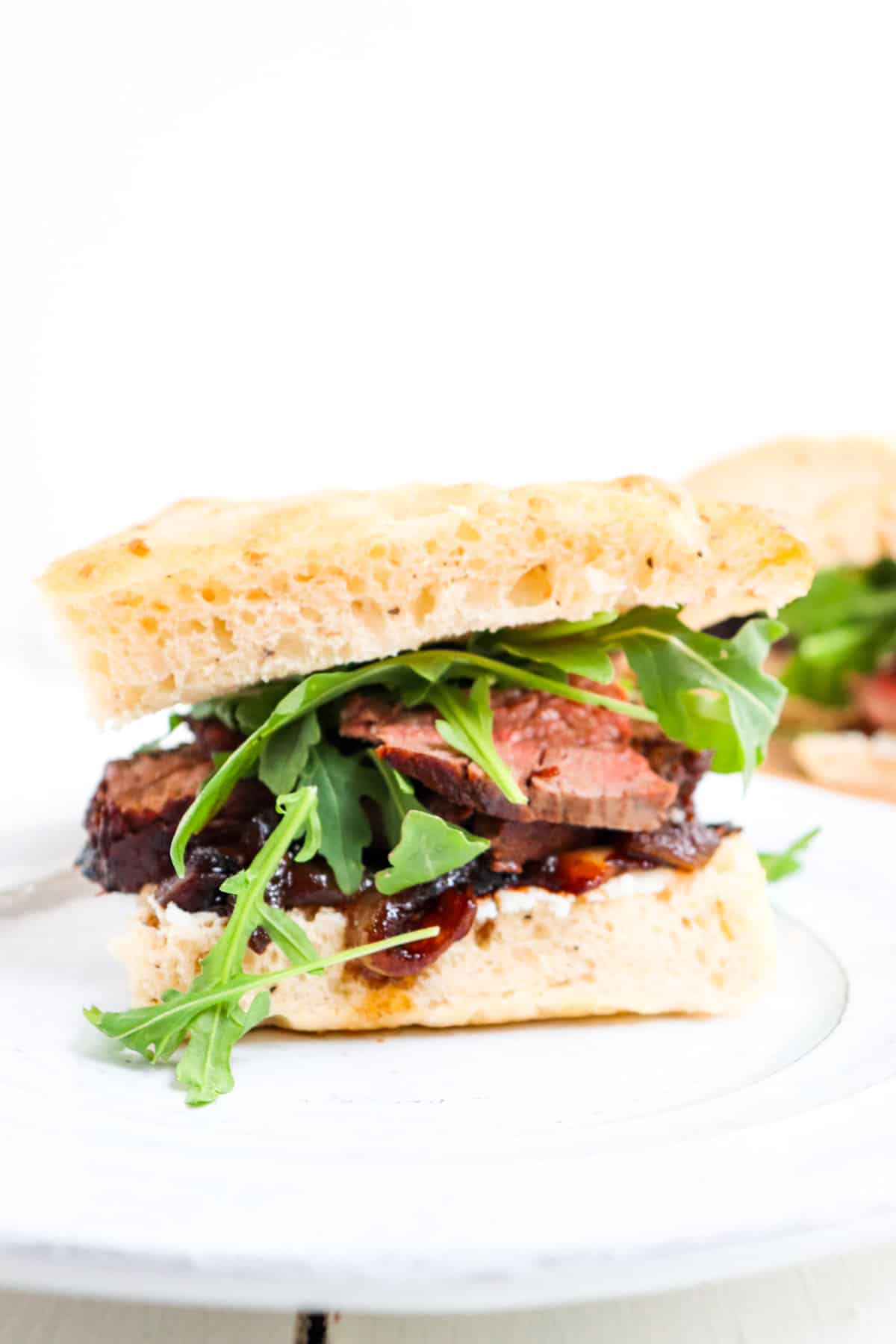 one steak and arugula sandwich on a plate.