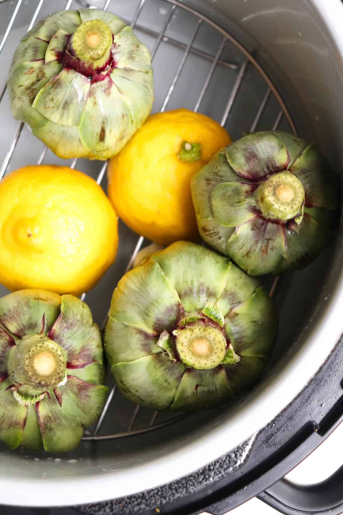 artichokes and lemons resting on trivet in instant pot.