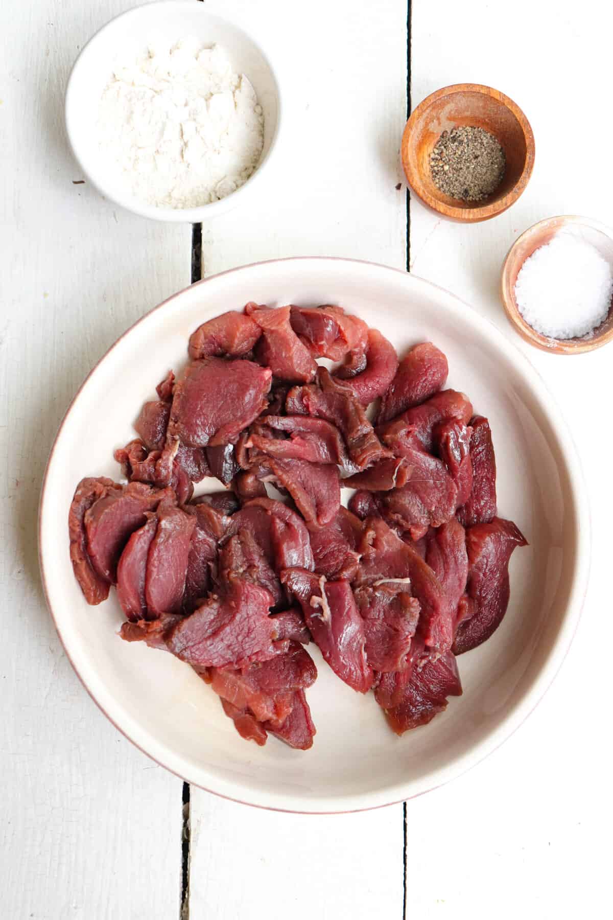 sliced deer meat with flour in the background.