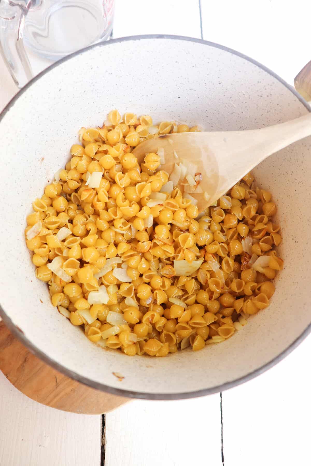 small shells and onions sauteed in a white pot.