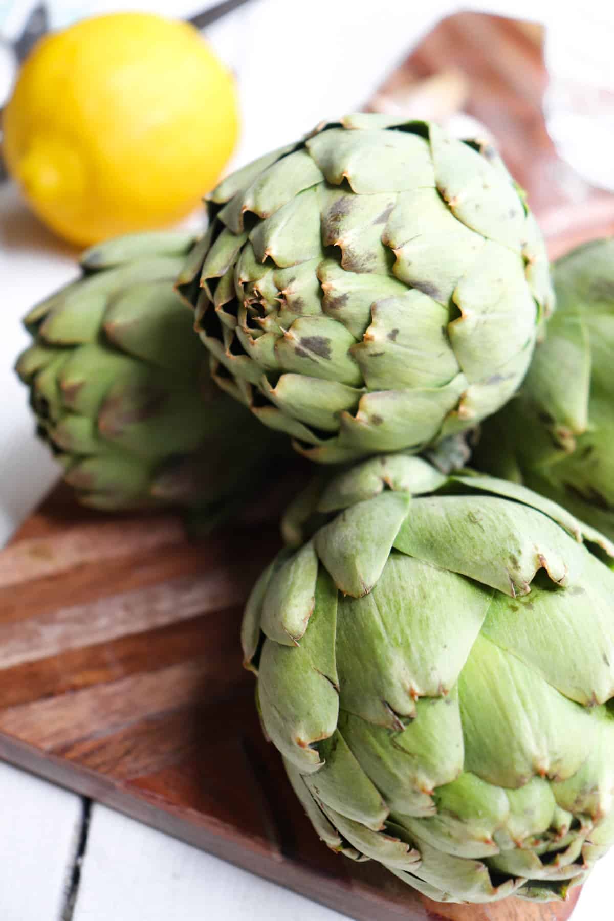 uncooked artichokes on a cutting board.