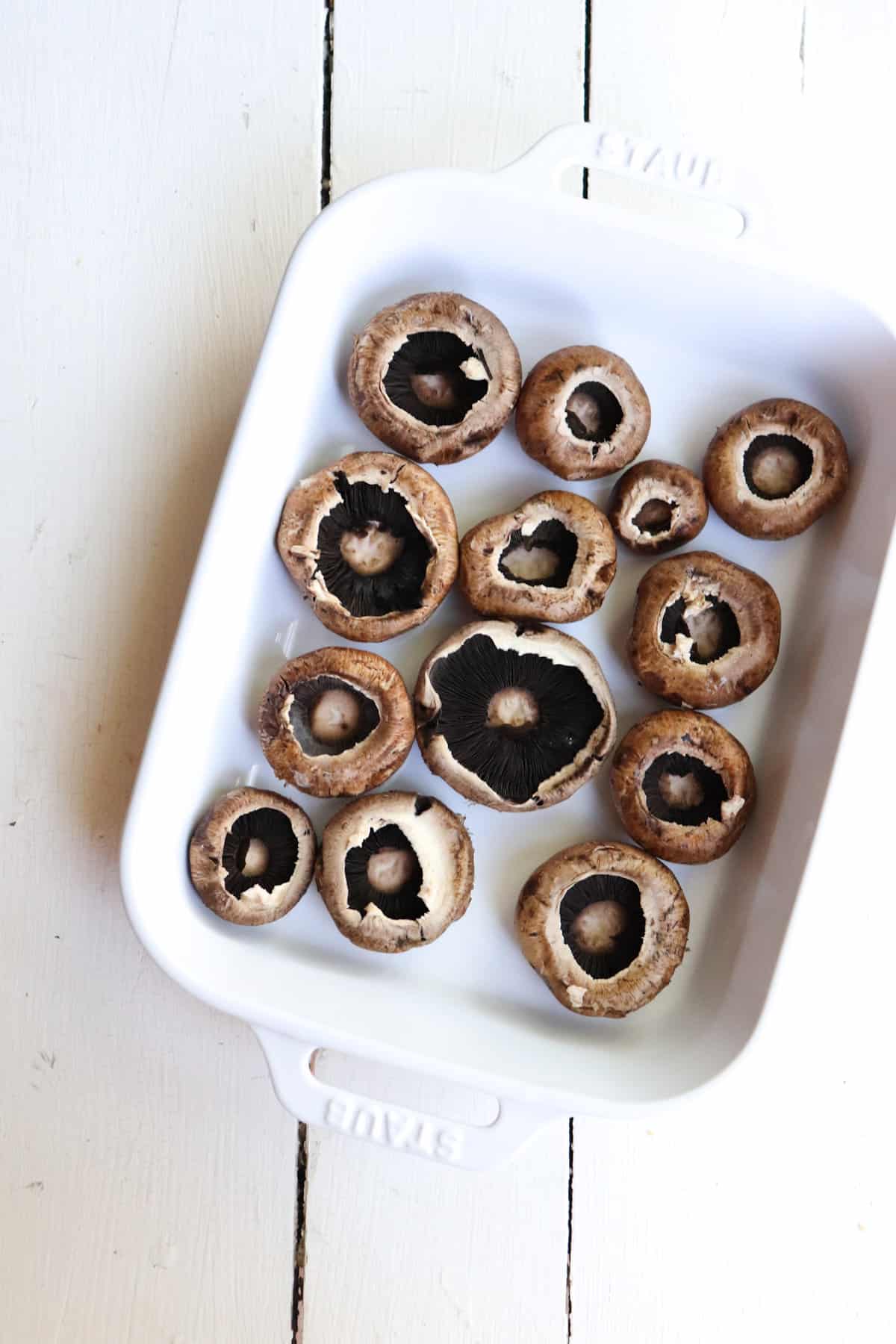 mushroom caps with stems removed in a white baking dish.