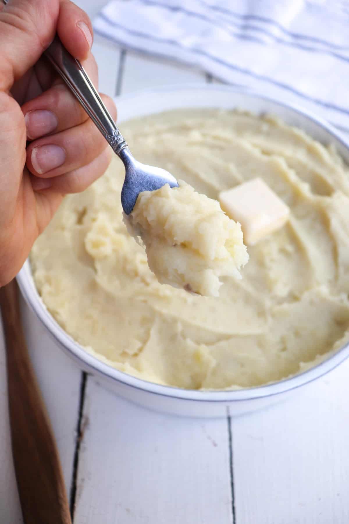 hand holding a forkful of mashed potatoes up to the camera.
