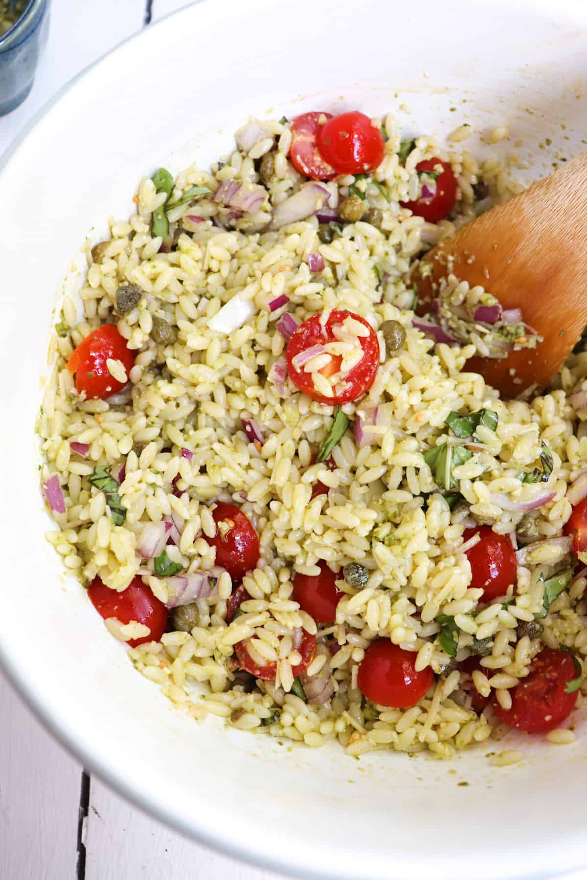 pesto orzo salad in a bowl with a wooden spoon.