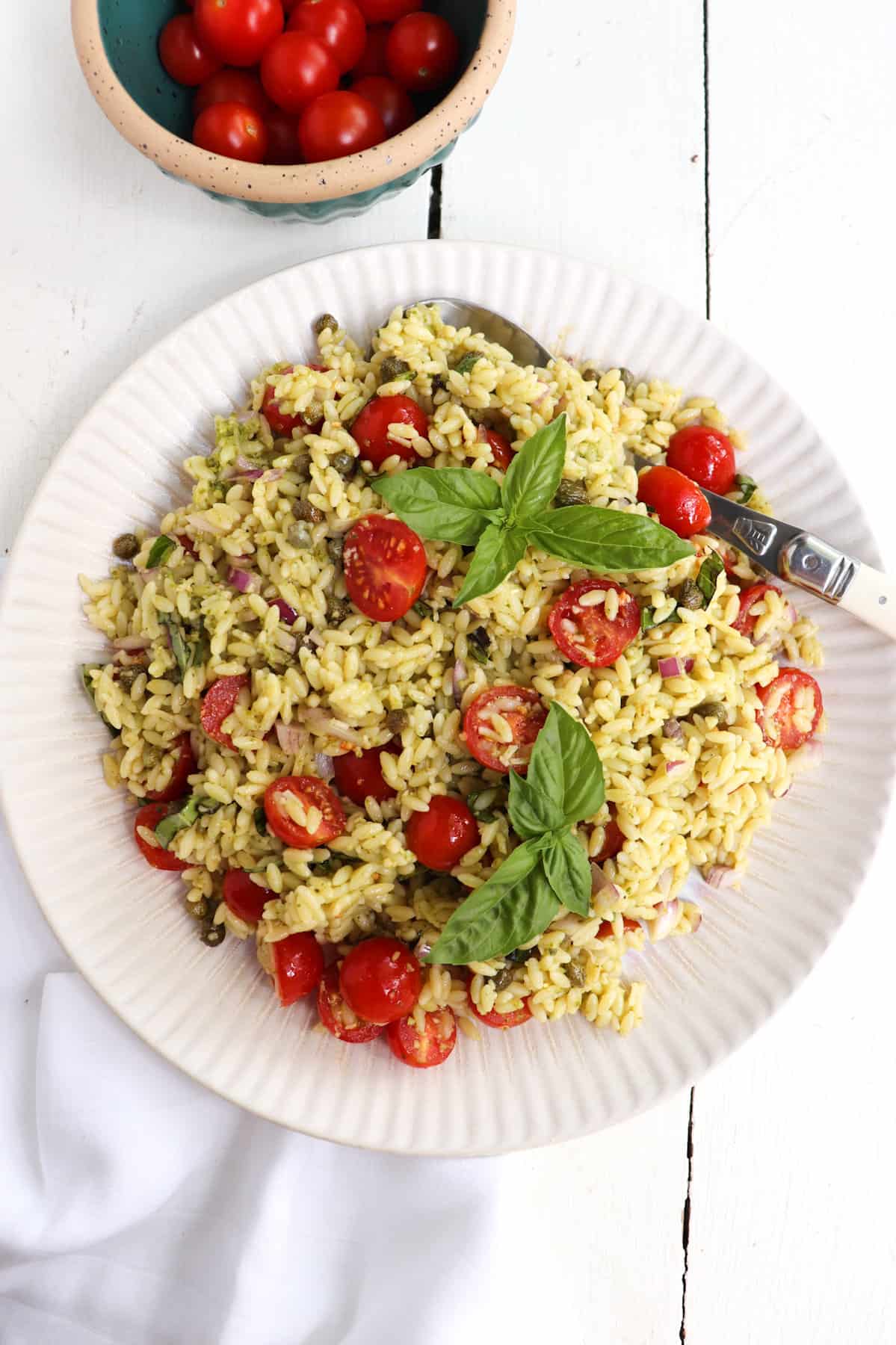 orzo pesto salad with tomatoes in a bowl on top and a white towel beneath.