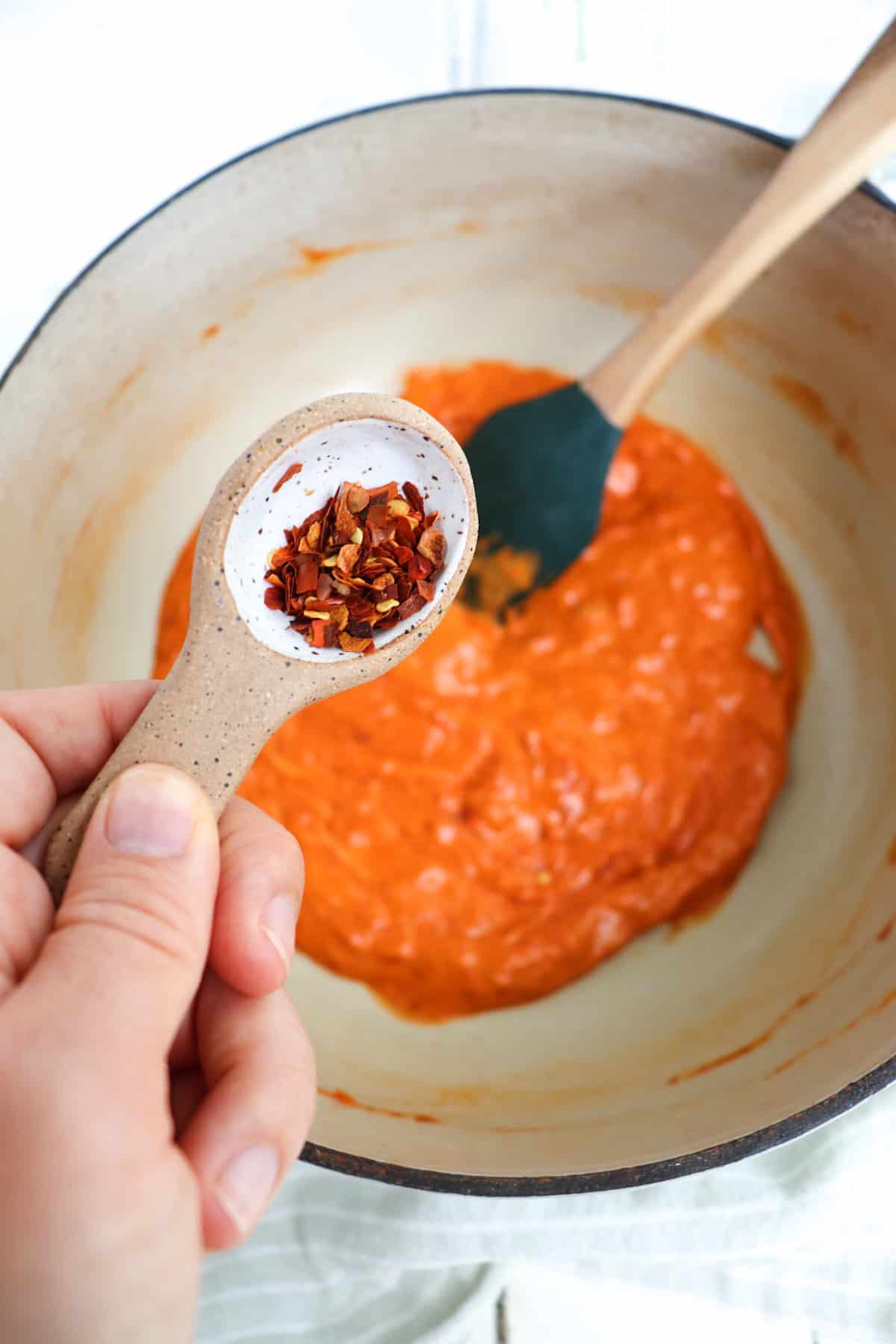 measuring spoon adding in red pepper flakes to sauce.